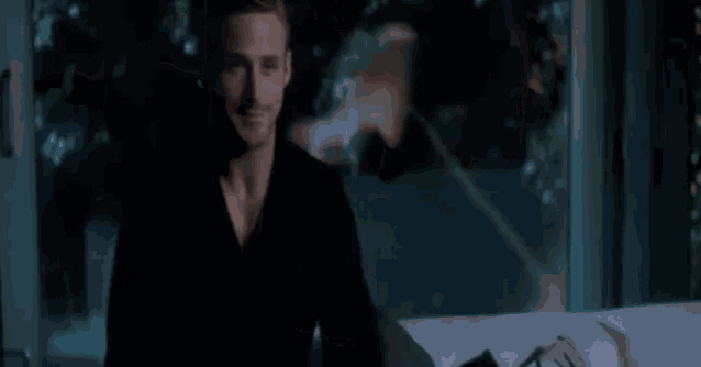 a man in a black shirt is sitting on a couch in front of a window in a dark room .