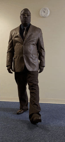 a man in a suit and tie stands in front of a wall clock that shows a time of 4:20