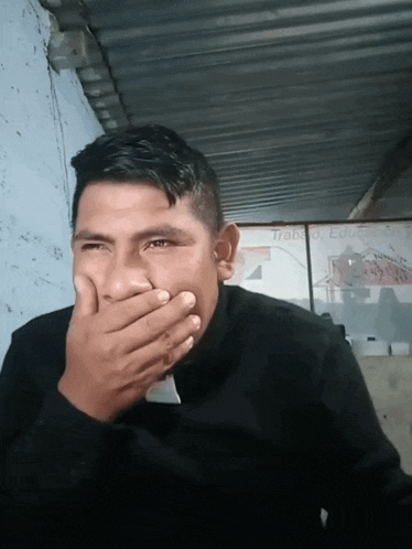 a man is covering his mouth with his hand in front of a sign that says trabajo educacion