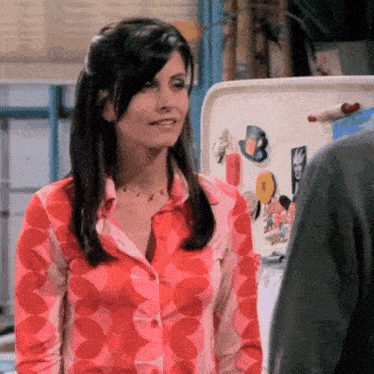 a woman in a red shirt stands in front of a refrigerator