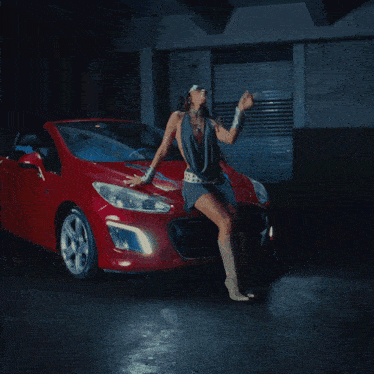 a woman sitting on the hood of a red sports car
