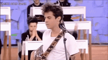 a man is singing into a microphone while playing a guitar in front of a crowd of people .