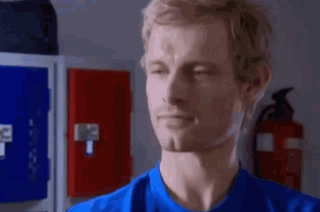 a man in a blue shirt is standing in front of a fire extinguisher in a locker room .