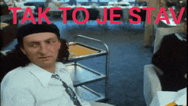 a man sitting in front of a cart with the words tak to je stav written in red letters