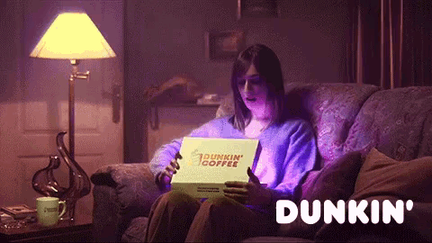 a woman sits on a couch holding a dunkin ' donut box