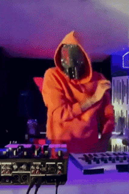 a man in an orange hoodie is standing in front of a mixer with his arms crossed
