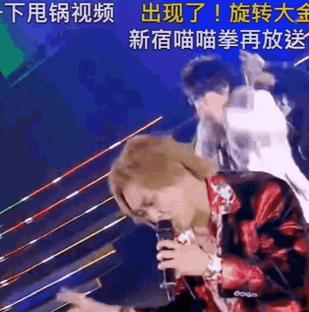 a man in a red jacket is singing into a microphone on a stage .