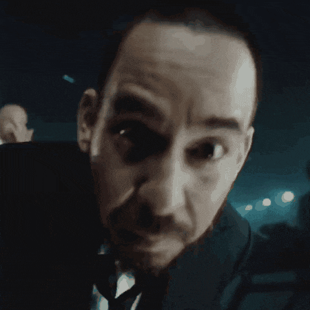 a man with a beard wearing a suit and tie looks at the camera