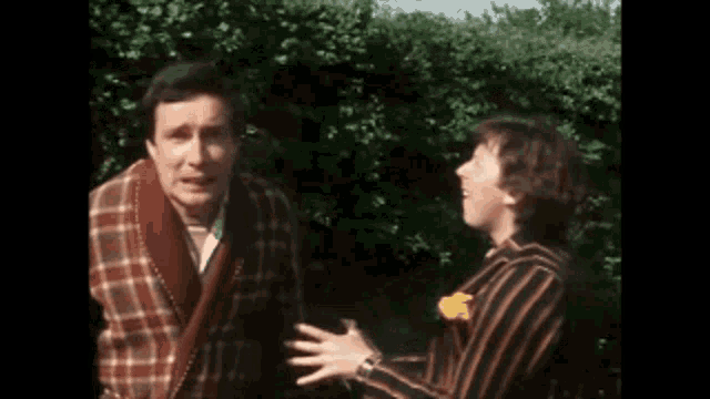 two men are standing next to each other in front of a hedge