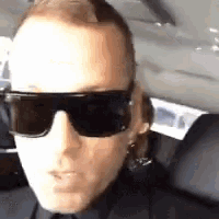 a man wearing sunglasses is sitting in a car and making a funny face .