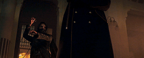 a man in a black coat is standing next to a woman in a black mask