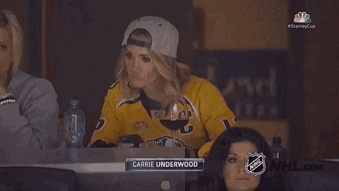 carrie underwood is sitting at a table with a glass of wine in her hand