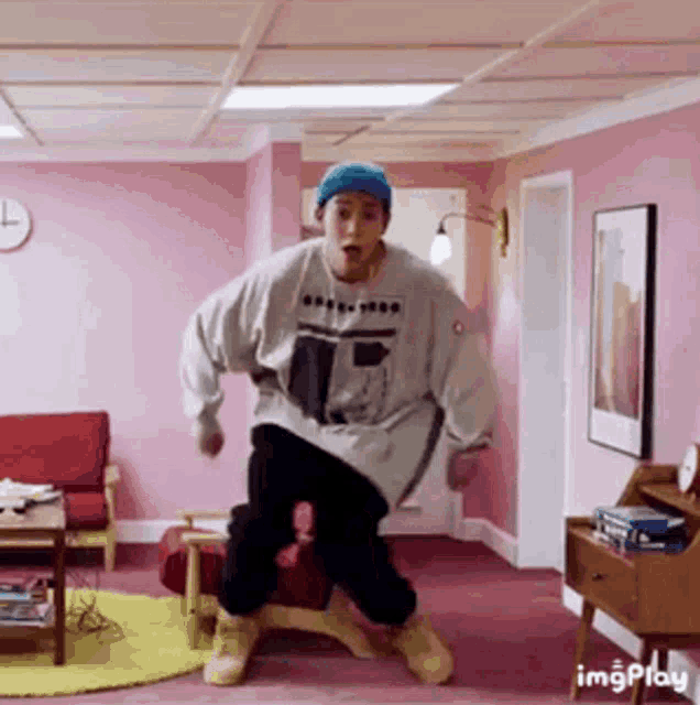 a man is dancing in a living room with pink walls and a blue hat .