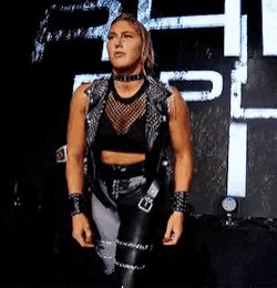 a woman in a leather vest and pants is standing in front of a sign that says rp .