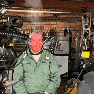 a man in a green jacket is standing in front of a welding machine that says ' powermatic ' on it