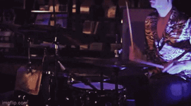 a man is playing drums in a dark room with a laptop in the background ..