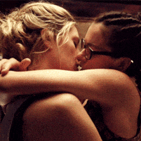 two women kissing with one wearing glasses and braids