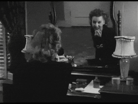 a black and white photo of a woman looking at her reflection in the mirror