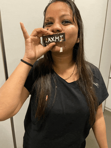 a woman in a black shirt holds a laxmi bar in front of her face