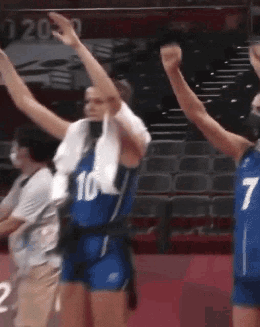 a woman wearing a blue number 10 jersey holds her arms up in the air