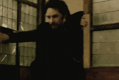 a man in a black suit is standing in front of a window with his arms outstretched