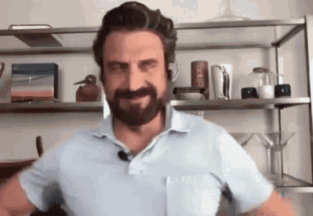 a man with a beard and mustache is standing in front of a shelf in a room .