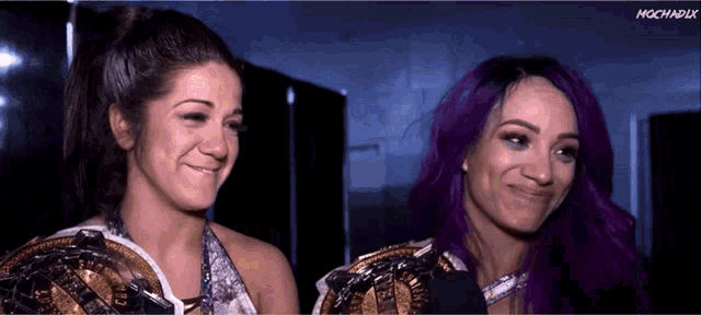 two women with purple hair are smiling in a dark room
