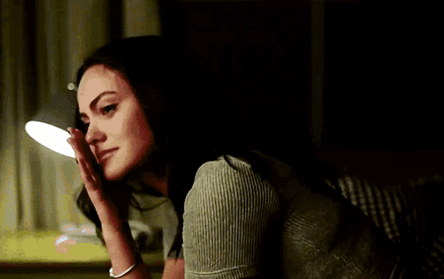 a woman sitting on a couch with her hand on her face and a lamp in the background