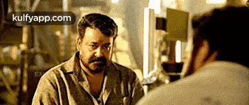 a man with a beard is looking at himself in a mirror with the website kulfyapp.com in the corner .