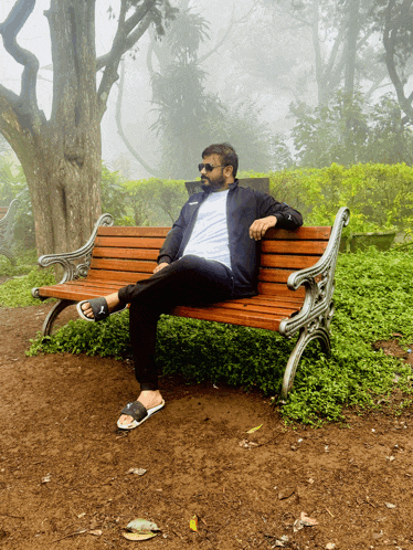 a man sits on a wooden bench with his legs crossed and wearing sandals