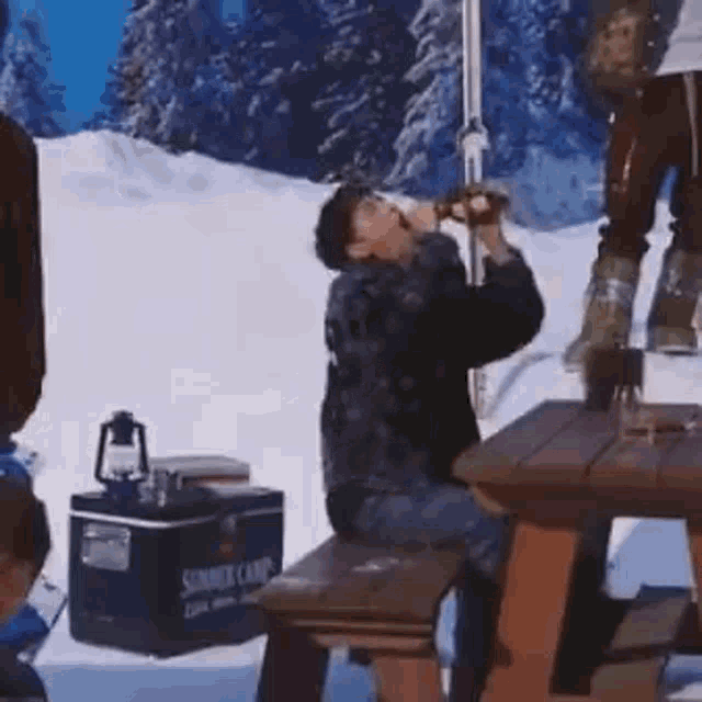 a man is sitting at a picnic table drinking from a bottle .