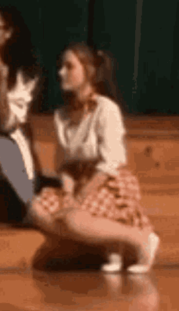 a woman in a plaid skirt is kneeling on the floor in a gym .