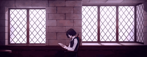 a man in a suit is sitting in front of a window reading a book