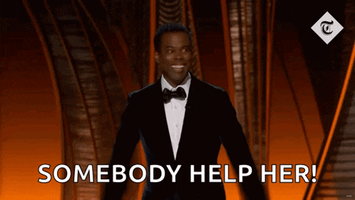 a man in a tuxedo is standing on a stage and says " somebody help her "
