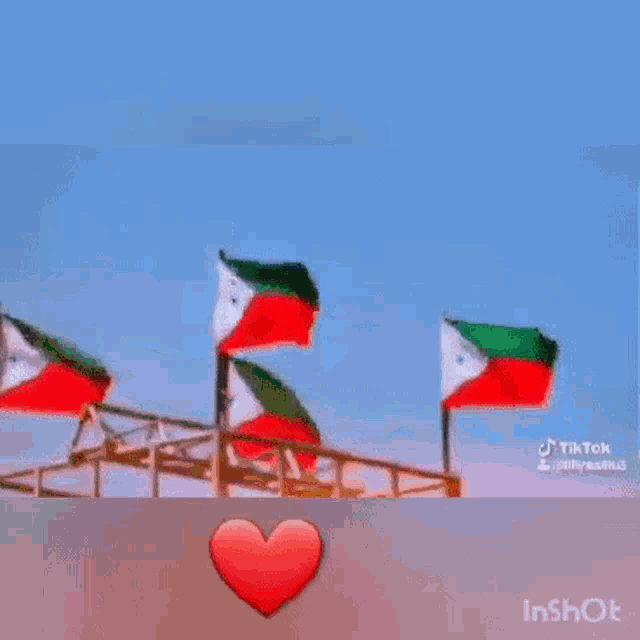 a red heart is in front of a tower with flags flying in the sky .