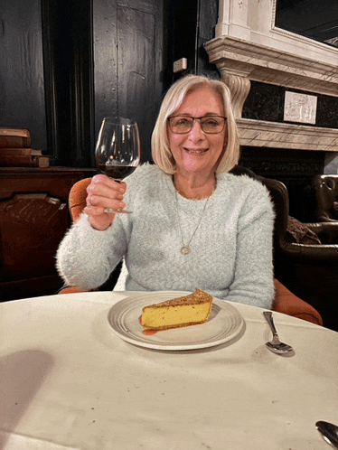 a woman sitting at a table with a glass of wine and a piece of pie on a plate