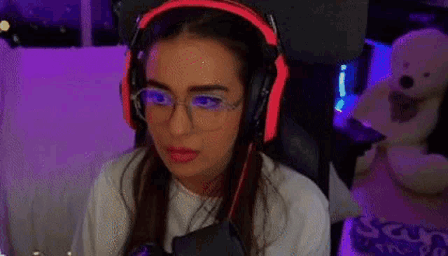 a woman wearing headphones and glasses is sitting in a chair in front of a teddy bear .