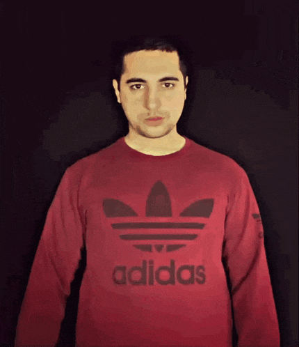 a man wearing a red adidas sweatshirt stands in front of a black background