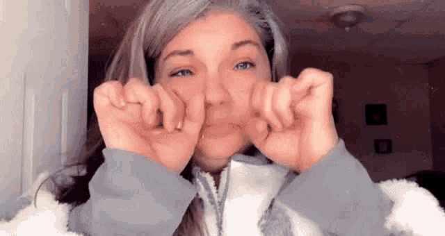 a woman is making a funny face with her hands while wearing a jacket .