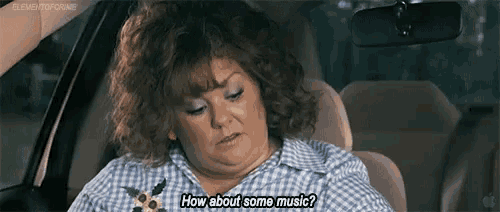 a woman is sitting in the driver 's seat of a car asking how about some music .