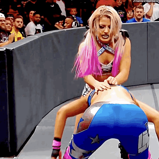 a woman with pink hair is wrestling another woman with blue shorts