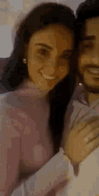 a man and a woman are hugging each other and smiling . the woman is wearing a pink sweater .