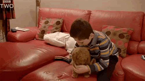 a boy is petting a dog on a red couch .