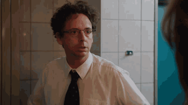 a man with curly hair and glasses looks at himself in a mirror