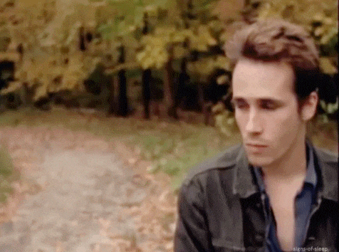 a man in a black jacket is standing in the woods looking at the camera .
