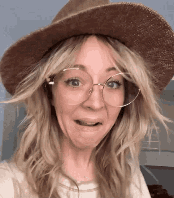 a woman wearing glasses and a hat makes a funny face