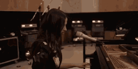 a woman is playing a piano and singing into a microphone in a recording studio .