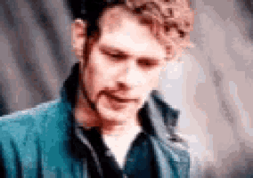 a man with curly hair and a beard is wearing a blue jacket and black shirt .