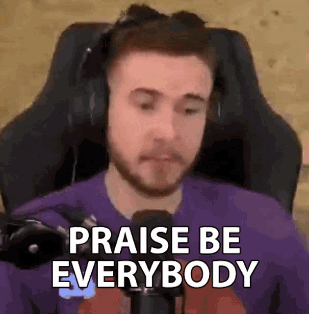 a man wearing headphones is sitting in front of a microphone and saying `` praise be everybody ''