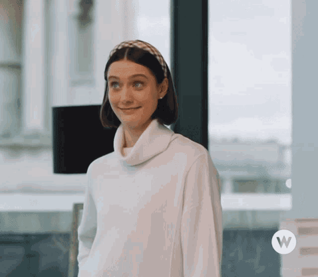a woman wearing a white sweater and a headband with the letter w on the bottom right